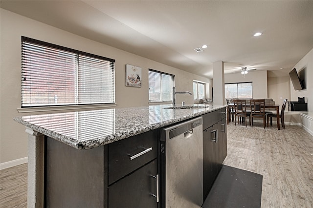 kitchen with stainless steel dishwasher, a sink, a center island with sink, light wood-type flooring, and baseboards