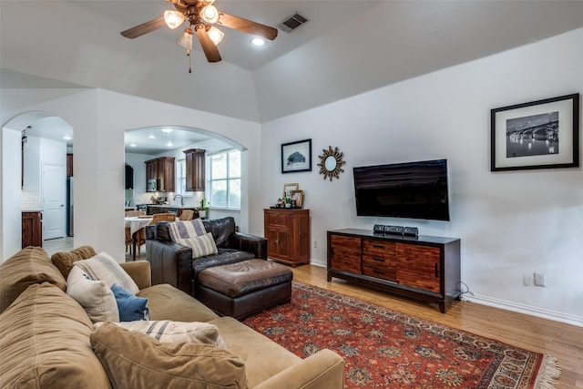 living room featuring light wood finished floors, visible vents, arched walkways, baseboards, and ceiling fan