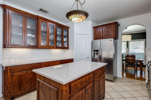 kitchen featuring arched walkways, tasteful backsplash, glass insert cabinets, stainless steel refrigerator with ice dispenser, and light tile patterned floors
