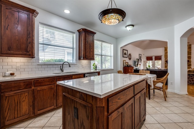 kitchen featuring light stone counters, a center island, a sink, light tile patterned floors, and backsplash