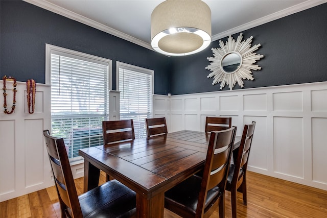 dining room featuring a textured wall, light wood-type flooring, a decorative wall, crown molding, and wainscoting