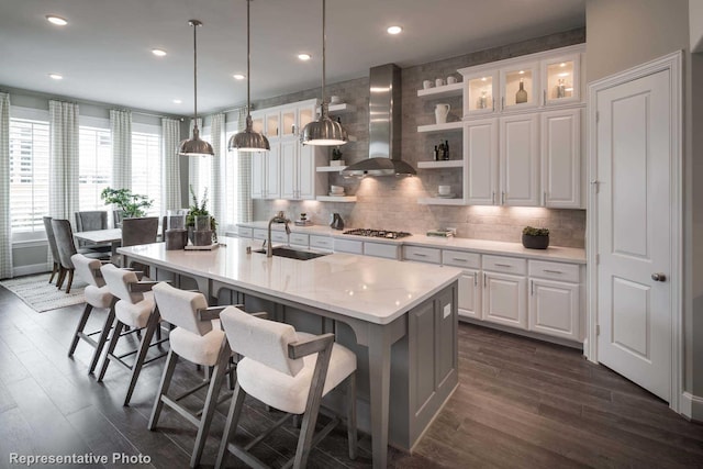 kitchen with wall chimney exhaust hood, stainless steel gas cooktop, a sink, open shelves, and light countertops