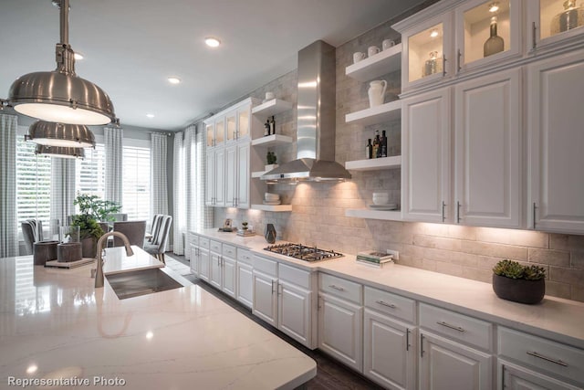 kitchen featuring wall chimney exhaust hood, a sink, white cabinetry, stainless steel gas stovetop, and open shelves