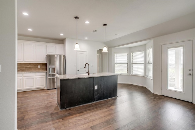 kitchen featuring white cabinets, wood finished floors, a sink, light stone countertops, and stainless steel refrigerator with ice dispenser