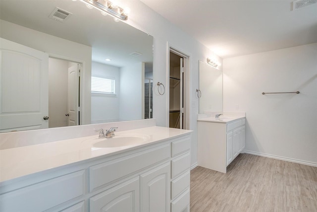 bathroom with two vanities, wood finished floors, visible vents, and a sink