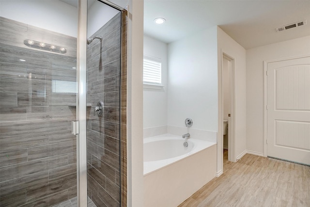 full bathroom featuring wood finished floors, visible vents, toilet, a garden tub, and a stall shower