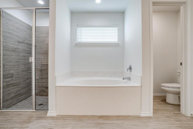 bathroom featuring a garden tub, wood finished floors, a shower stall, and toilet