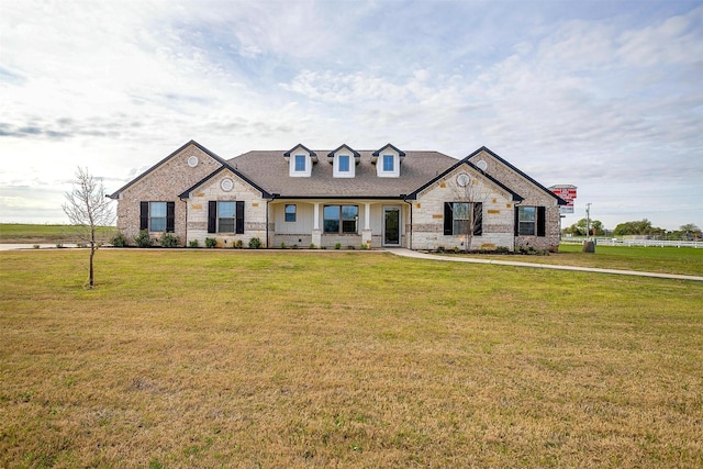 cape cod home featuring a front lawn, roof with shingles, and stone siding