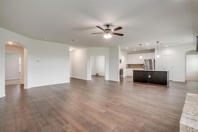 unfurnished living room featuring ceiling fan, arched walkways, baseboards, dark wood-style floors, and recessed lighting