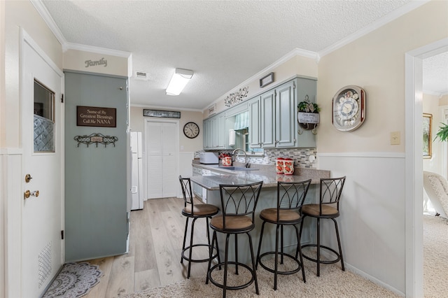 kitchen with a peninsula, a textured ceiling, a kitchen breakfast bar, and ornamental molding