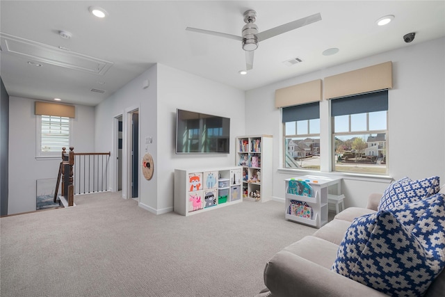 living area featuring attic access, baseboards, a ceiling fan, and carpet flooring