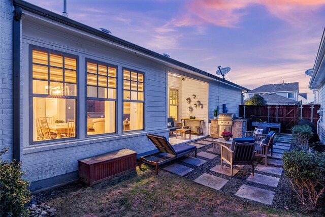 back of house at dusk with brick siding, an outdoor hangout area, a patio, and fence