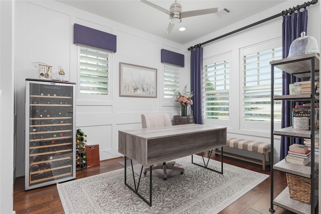 office featuring a decorative wall, wood finished floors, ceiling fan, visible vents, and wine cooler