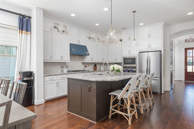 kitchen with arched walkways, appliances with stainless steel finishes, under cabinet range hood, and recessed lighting