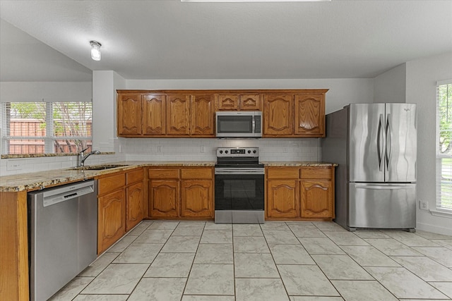 kitchen featuring brown cabinetry, appliances with stainless steel finishes, tasteful backsplash, and a sink