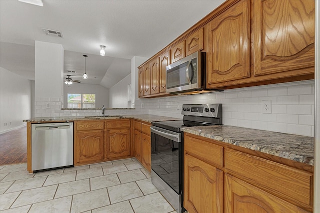 kitchen featuring brown cabinets, appliances with stainless steel finishes, decorative backsplash, and a sink