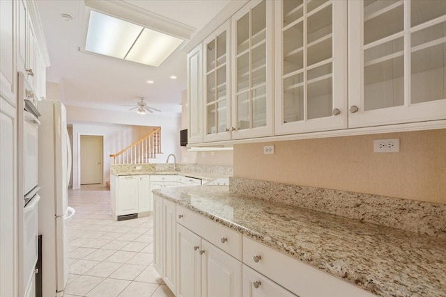 kitchen with light stone counters, a sink, glass insert cabinets, ceiling fan, and a peninsula
