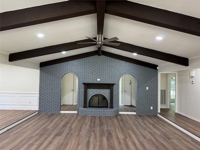 unfurnished living room featuring arched walkways, brick wall, a brick fireplace, wood finished floors, and ceiling fan