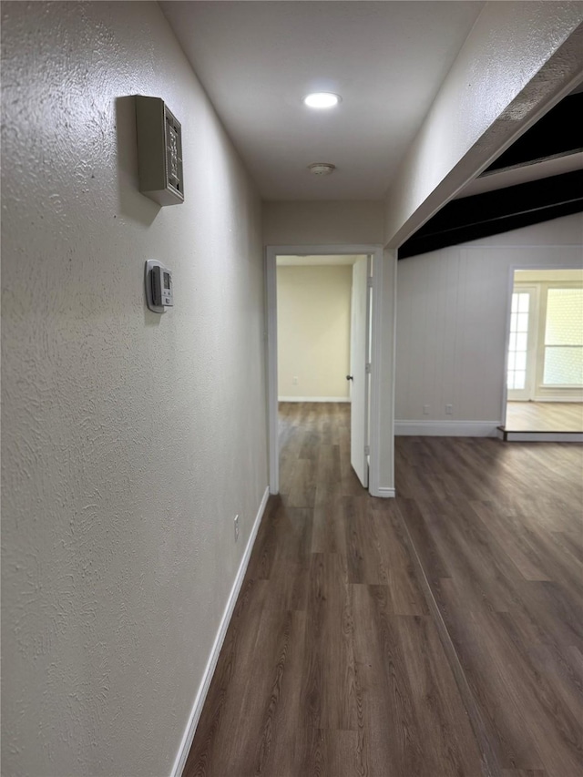 hallway featuring wood finished floors, baseboards, and a textured wall