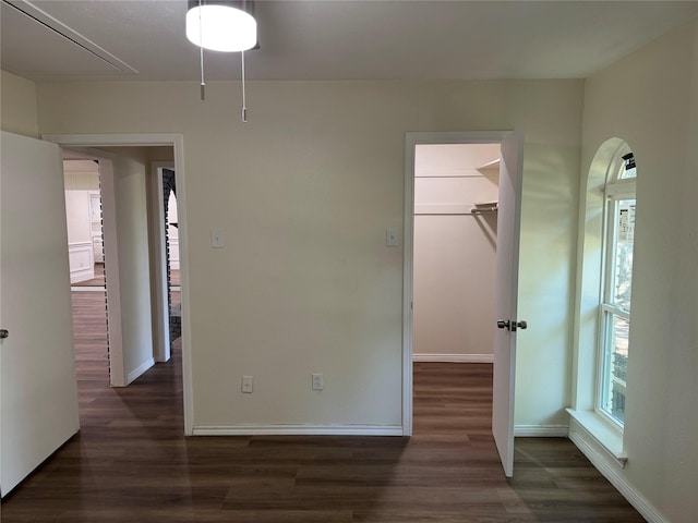 unfurnished bedroom featuring attic access, baseboards, a walk in closet, and wood finished floors