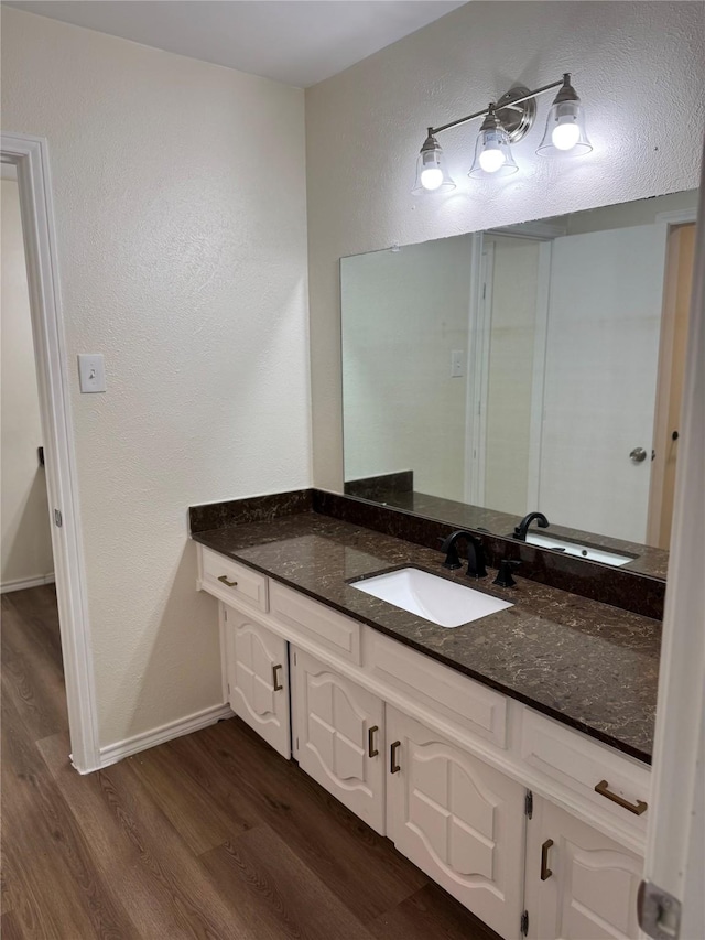 bathroom with baseboards, wood finished floors, a textured wall, and vanity