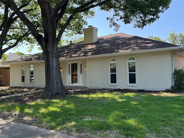 ranch-style house with a chimney, a front lawn, brick siding, and roof with shingles