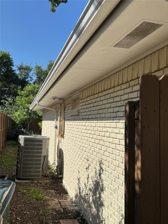 view of side of home featuring brick siding, central air condition unit, and fence