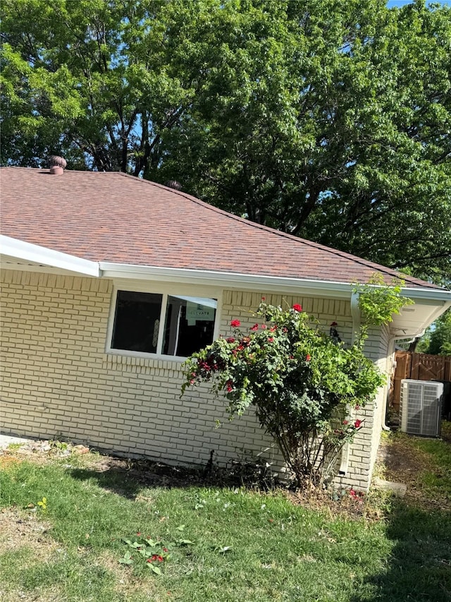 view of side of property with fence, brick siding, roof with shingles, and central air condition unit