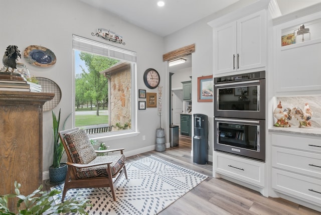 kitchen featuring white cabinets, double wall oven, baseboards, and light wood-style floors