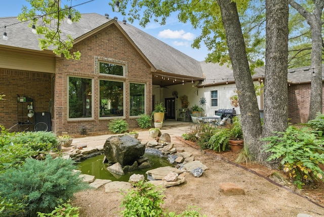rear view of house featuring brick siding, a small pond, a patio area, and a shingled roof