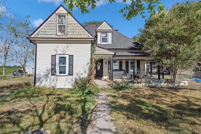 view of front facade with a front yard, a shingled roof, and covered porch
