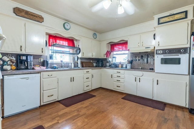 kitchen featuring white cabinets, under cabinet range hood, a sink, white appliances, and ceiling fan