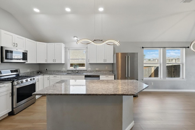 kitchen featuring a sink, stainless steel appliances, lofted ceiling, light stone countertops, and a kitchen island