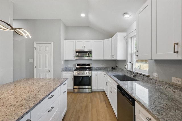 kitchen featuring lofted ceiling, light wood finished floors, stainless steel appliances, a sink, and white cabinetry