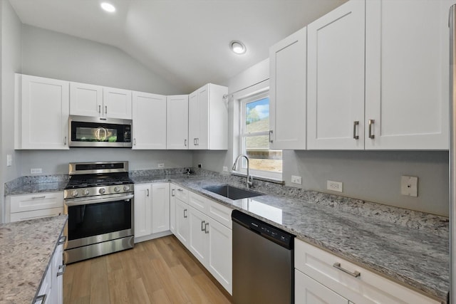 kitchen featuring white cabinets, lofted ceiling, stainless steel appliances, a sink, and light wood-style floors