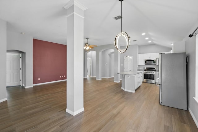 kitchen with white cabinets, stainless steel appliances, vaulted ceiling, arched walkways, and open floor plan