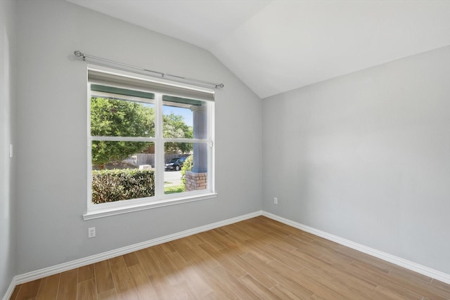spare room featuring vaulted ceiling, baseboards, and light wood-style floors