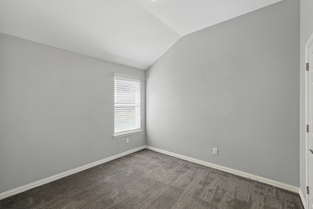 empty room featuring lofted ceiling, baseboards, and dark carpet