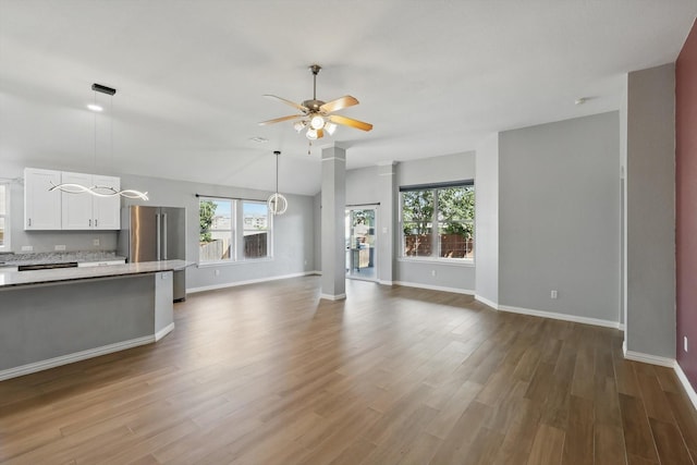 unfurnished living room with a wealth of natural light, a ceiling fan, dark wood-type flooring, and baseboards