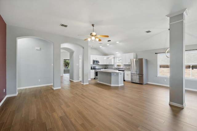 unfurnished living room with vaulted ceiling, visible vents, a wealth of natural light, and ceiling fan