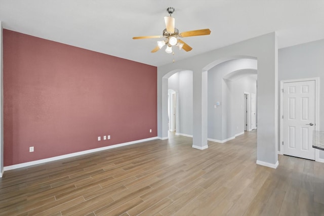 empty room featuring a ceiling fan, baseboards, arched walkways, and light wood-style flooring