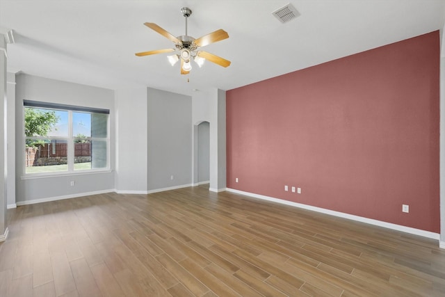 unfurnished room with wood finished floors, a ceiling fan, visible vents, and arched walkways