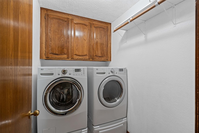 washroom featuring cabinet space, a textured ceiling, and washing machine and dryer