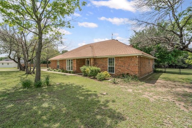 back of property with brick siding, fence, a shingled roof, and a yard