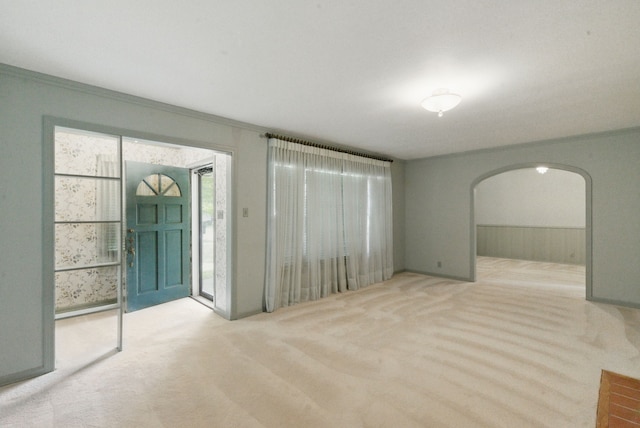 unfurnished living room with arched walkways, carpet floors, a wainscoted wall, and ornamental molding