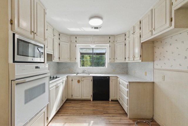 kitchen featuring light wood-style flooring, a sink, visible vents, backsplash, and black appliances