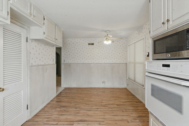 kitchen featuring stainless steel microwave, white oven, visible vents, wallpapered walls, and a ceiling fan
