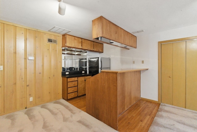 kitchen featuring wood finished floors, visible vents, freestanding refrigerator, a peninsula, and brown cabinetry