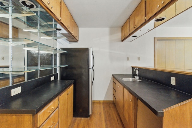 kitchen featuring brown cabinetry, dark countertops, a sink, and light wood-type flooring