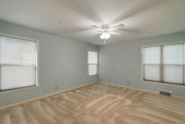 carpeted spare room featuring baseboards, a ceiling fan, visible vents, and ornamental molding